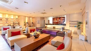 A modern hotel lobby with a reception desk, seating area, and a large coffee table.
