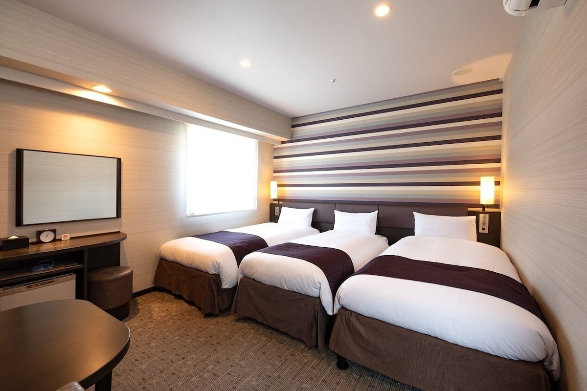 Ein Hotelzimmer mit zwei Betten, einem Schreibtisch, einem Sessel, einem Fernseher und einer gestreiften Wand.