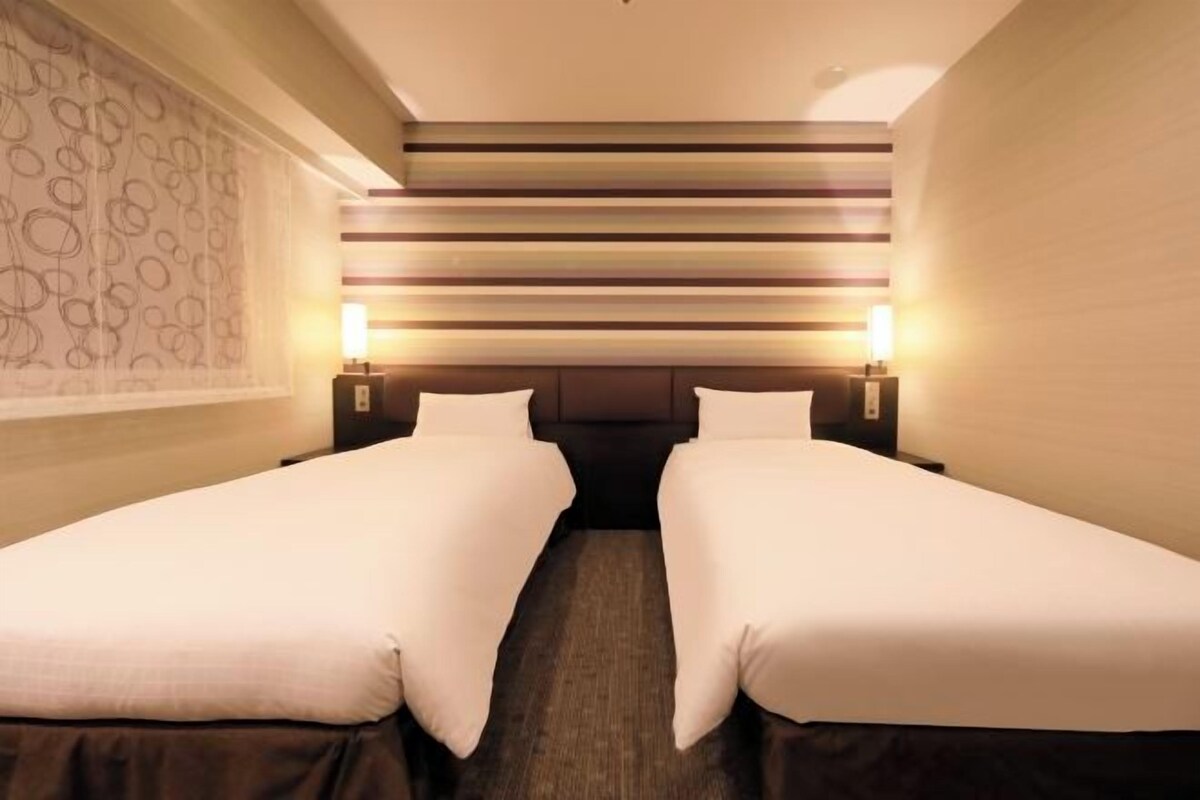 A hotel room with two single beds, a patterned wall, and a striped headboard.