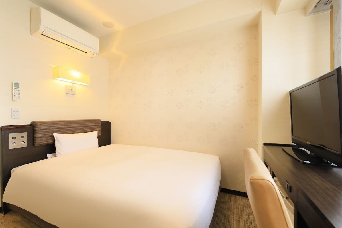 Ein Hotelzimmer mit einem Bett, einem Fernseher, einem Schreibtisch und einer Wandklimaanlage.