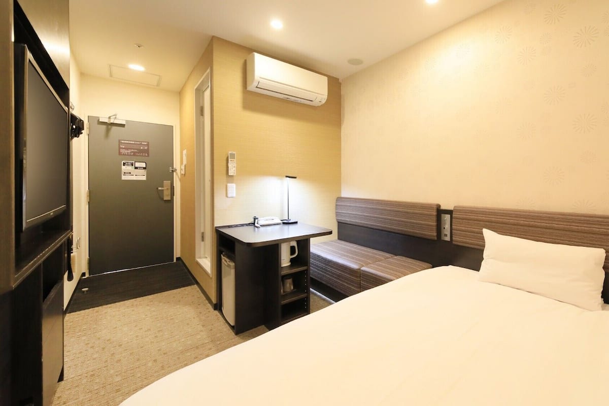 Ein Hotelzimmer mit Bett, Schreibtisch, Fernseher und Klimaanlage.