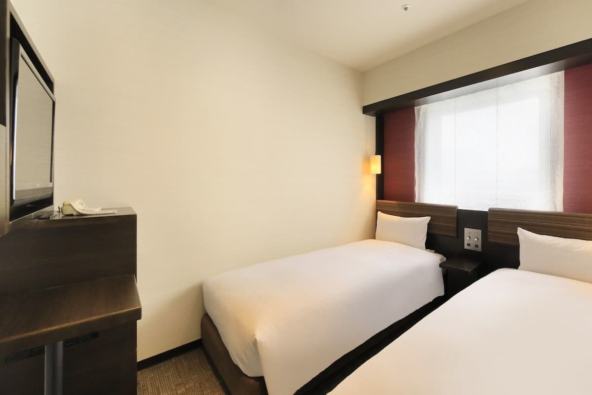 Ein Hotelzimmer mit zwei Betten, einem Schreibtisch mit Telefon und einem Fenster mit Vorhängen.