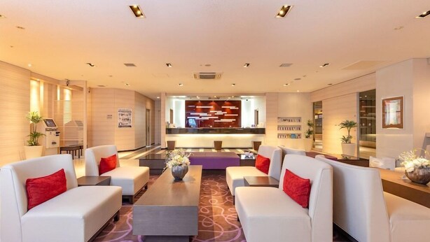 A modern hotel lobby with white sofas, a central coffee table, and a reception desk.