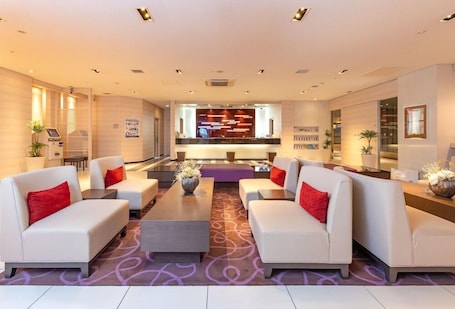 A modern hotel lobby with white sofas, a central coffee table, and a reception desk.