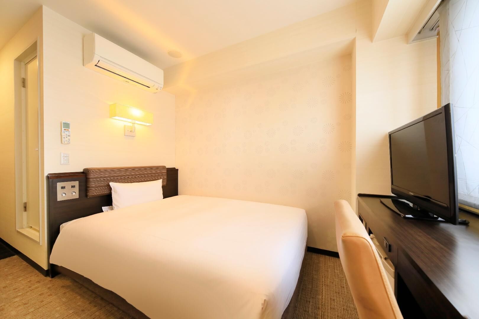 Habitació d'hotel amb llit, escriptori amb televisió, aire condicionat i làmpada penjada a la paret.