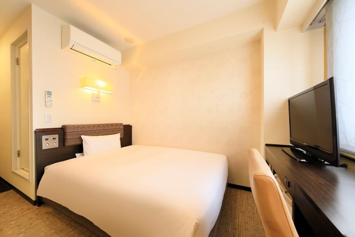 Ein Hotelzimmer mit einem Bett, einem Schreibtisch mit Fernseher, einer Klimaanlage und einer Wandleuchte.