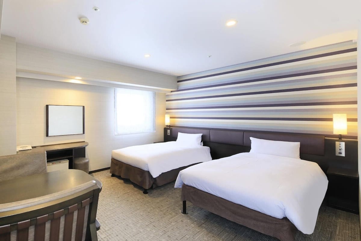 Ein Hotelzimmer mit zwei Betten, einem Schreibtisch, einem Stuhl, einem Fernseher und einer gestreiften Wand.