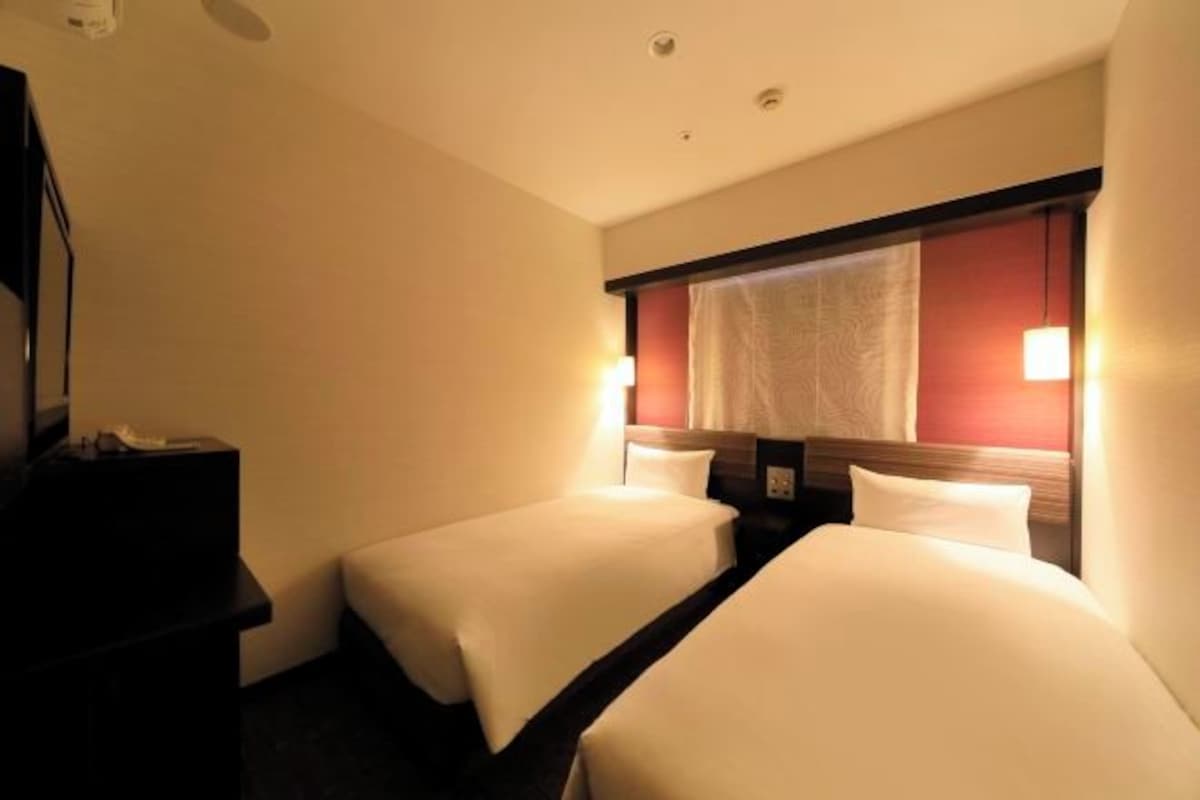 A hotel room with two beds, a desk, and a window with curtains.