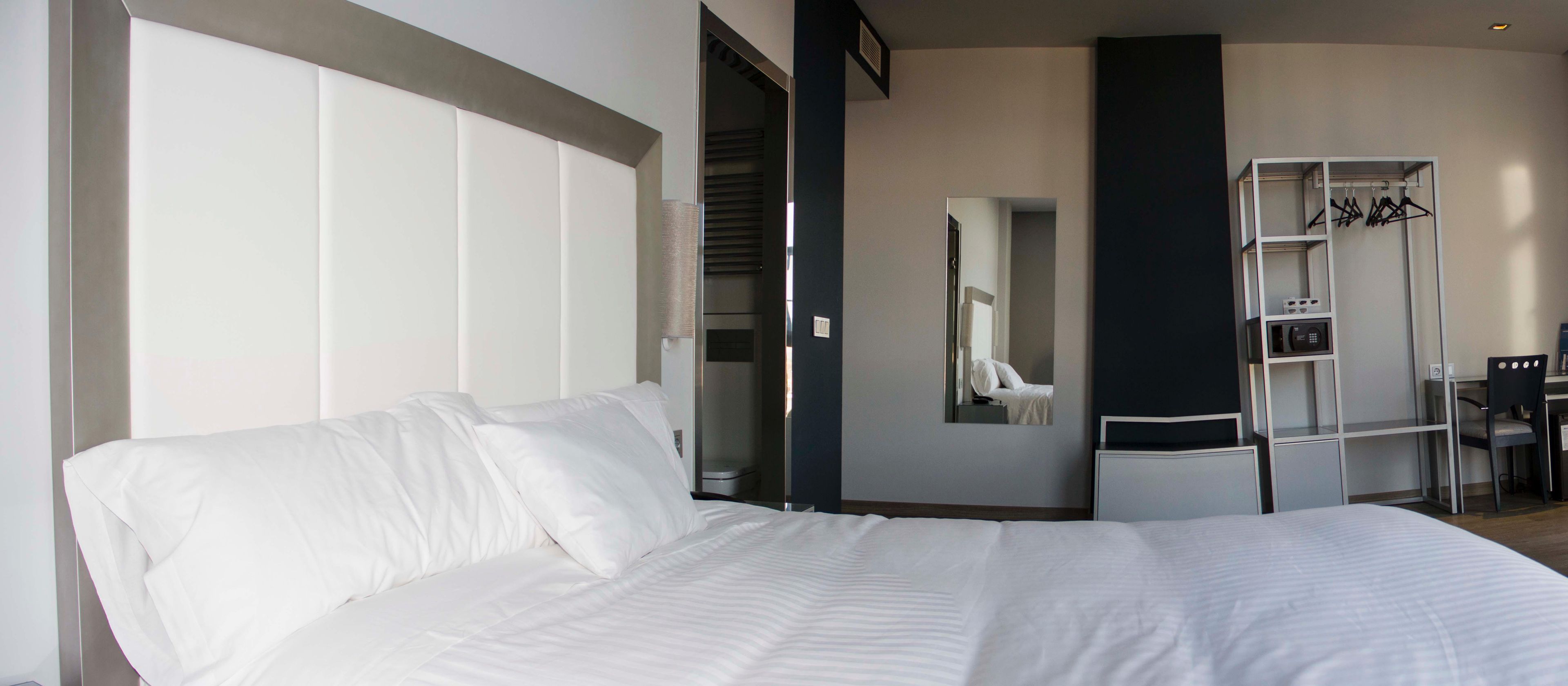 A hotel room with a large bed, a wardrobe, a mirror, and a desk.