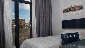 Une chambre d’hôtel avec un lit, une table en verre et une vue sur les immeubles, visible à travers une porte coulissante.