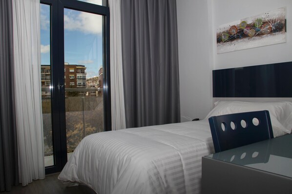 Een hotelkamer met een bed, een glazen tafel en een uitzicht op gebouwen door een schuifdeur.