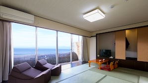 A modern hotel room with a large sliding glass door leading to a balcony, a sofa, a small table, and a television. - Ooedo Onsen Monogatari Toi Marine Hotel (Izu)