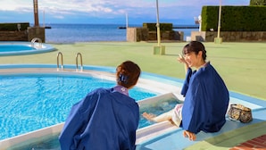 A pool area with a view of the sea, a lounge chair, and a small table with a bag. - Ooedo Onsen Monogatari Toi Marine Hotel (Izu)
