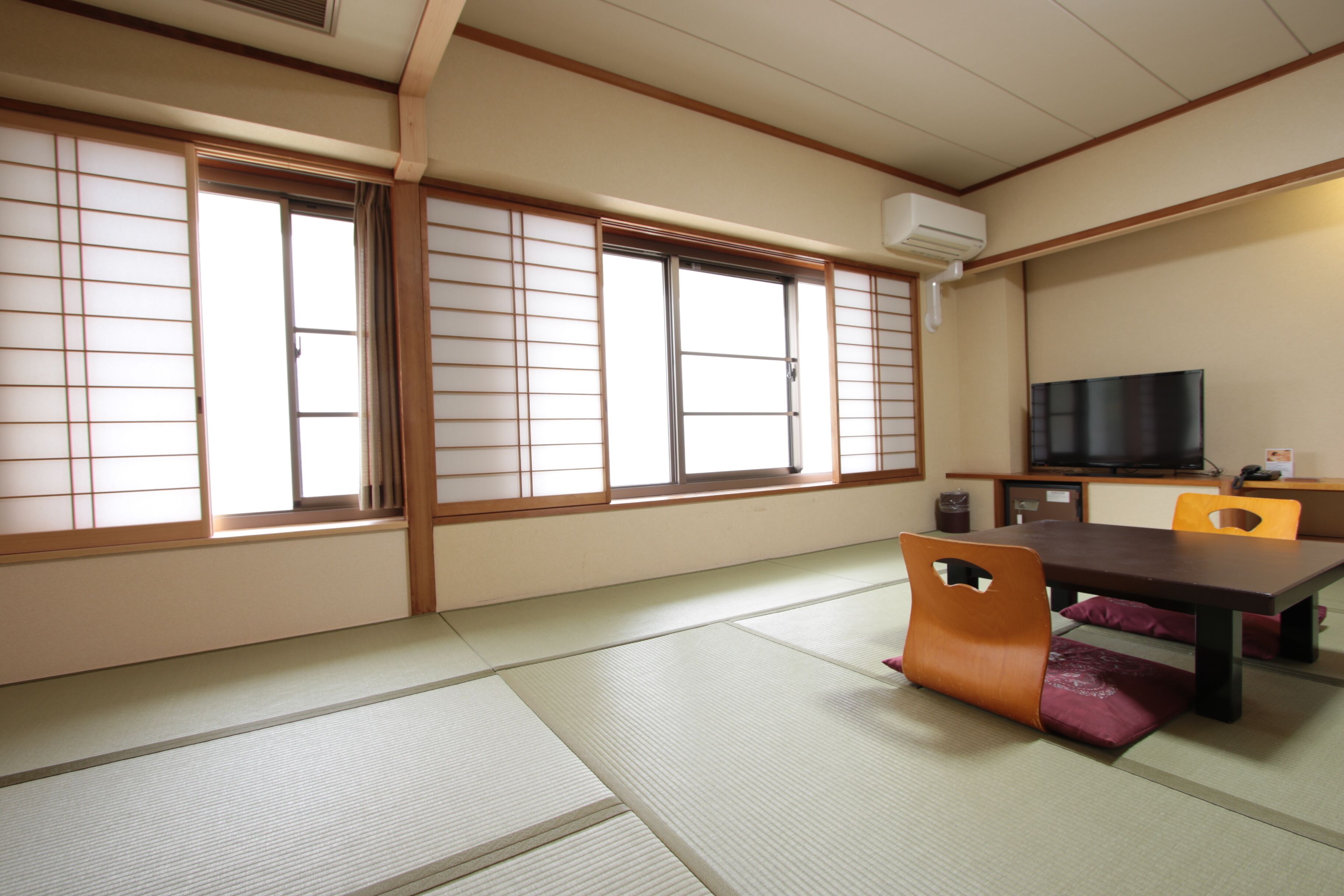A traditional Japanese room with tatami flooring, sliding shoji doors, a television, and a low table with cushions.