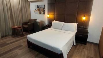 A modern hotel room with a large bed, a desk, a chair, and an air conditioning unit.