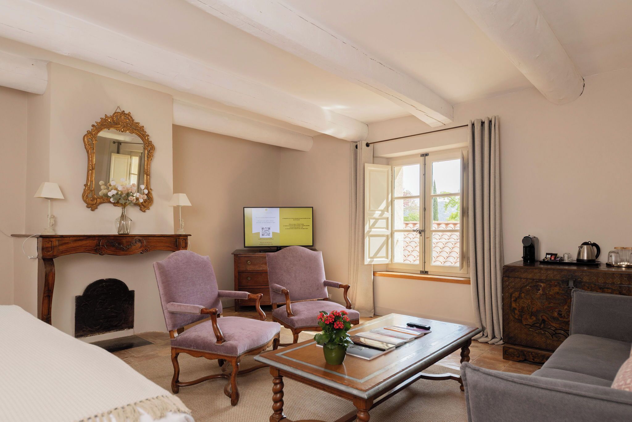 A hotel room with a bed, two armchairs, a coffee table, a fireplace, a television, and a window with curtains.