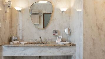A bathroom with a marble sink, two wall-mounted lights, a mirror, and a towel rack.