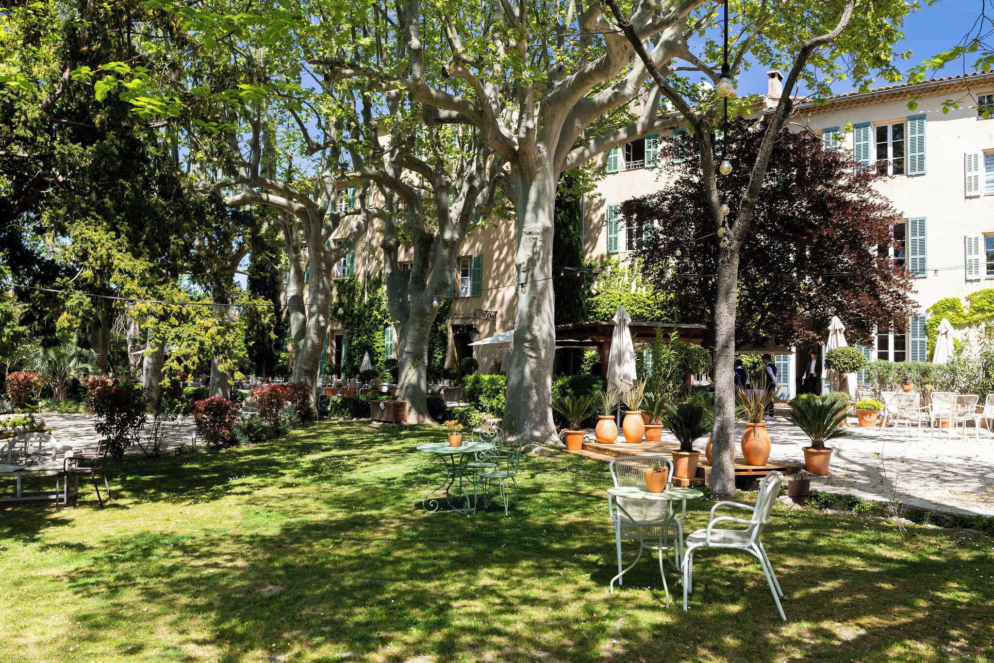 A garden with outdoor seating, large trees, and a building in the background.
