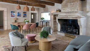 A spacious living area with a stone fireplace, wooden beams, a dining set, and comfortable seating. - Hotel Restaurant & Spa La Magdeleine - Mathias Dandine (Gemenos)