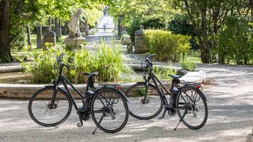 Two bicycles parked on a gravel path in a park with statues and a fountain in the background.