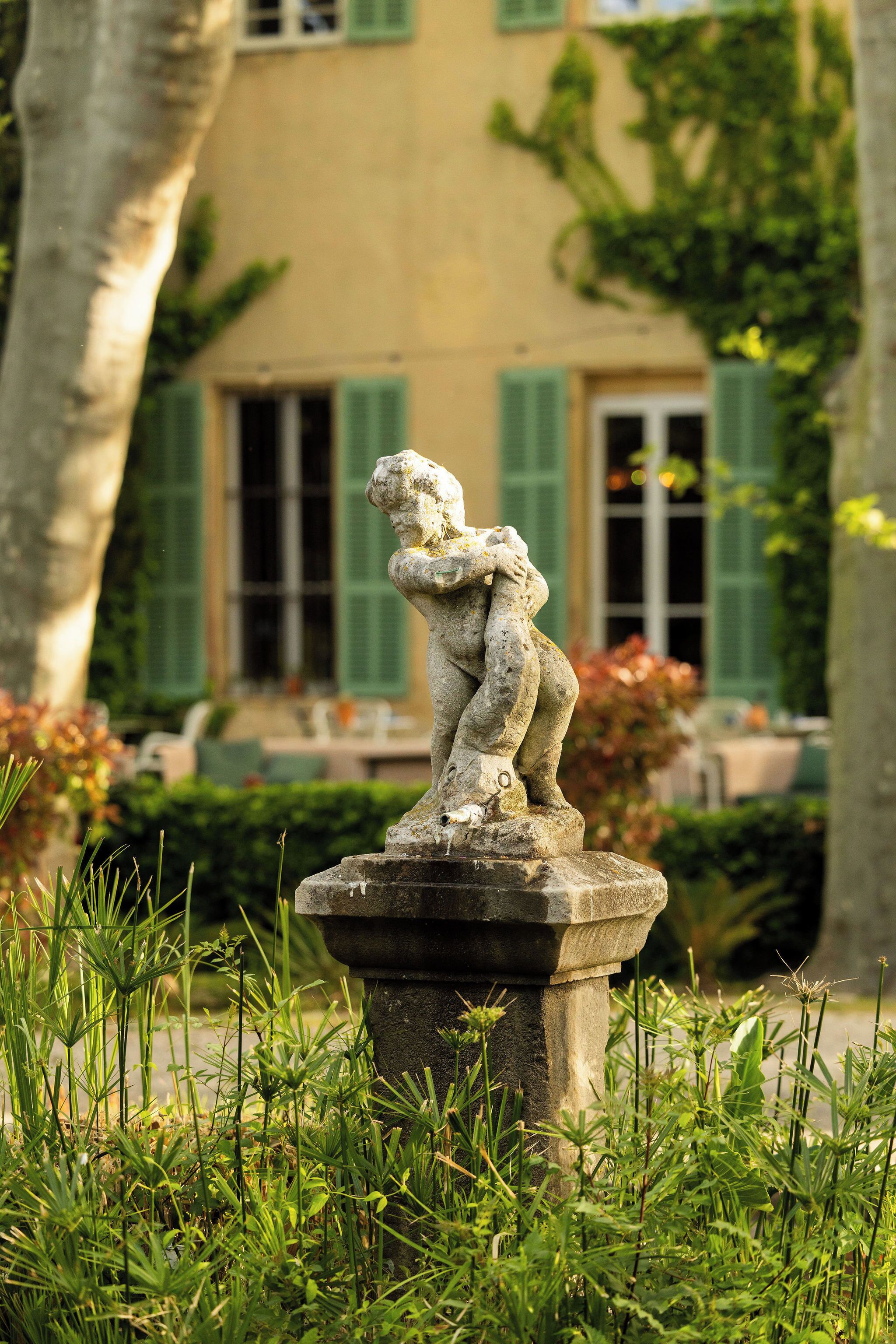 A stone sculpture of a child in a garden with a building in the background.