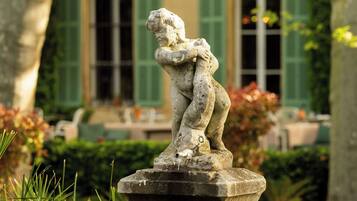 A stone sculpture of a child in a garden with a building in the background.