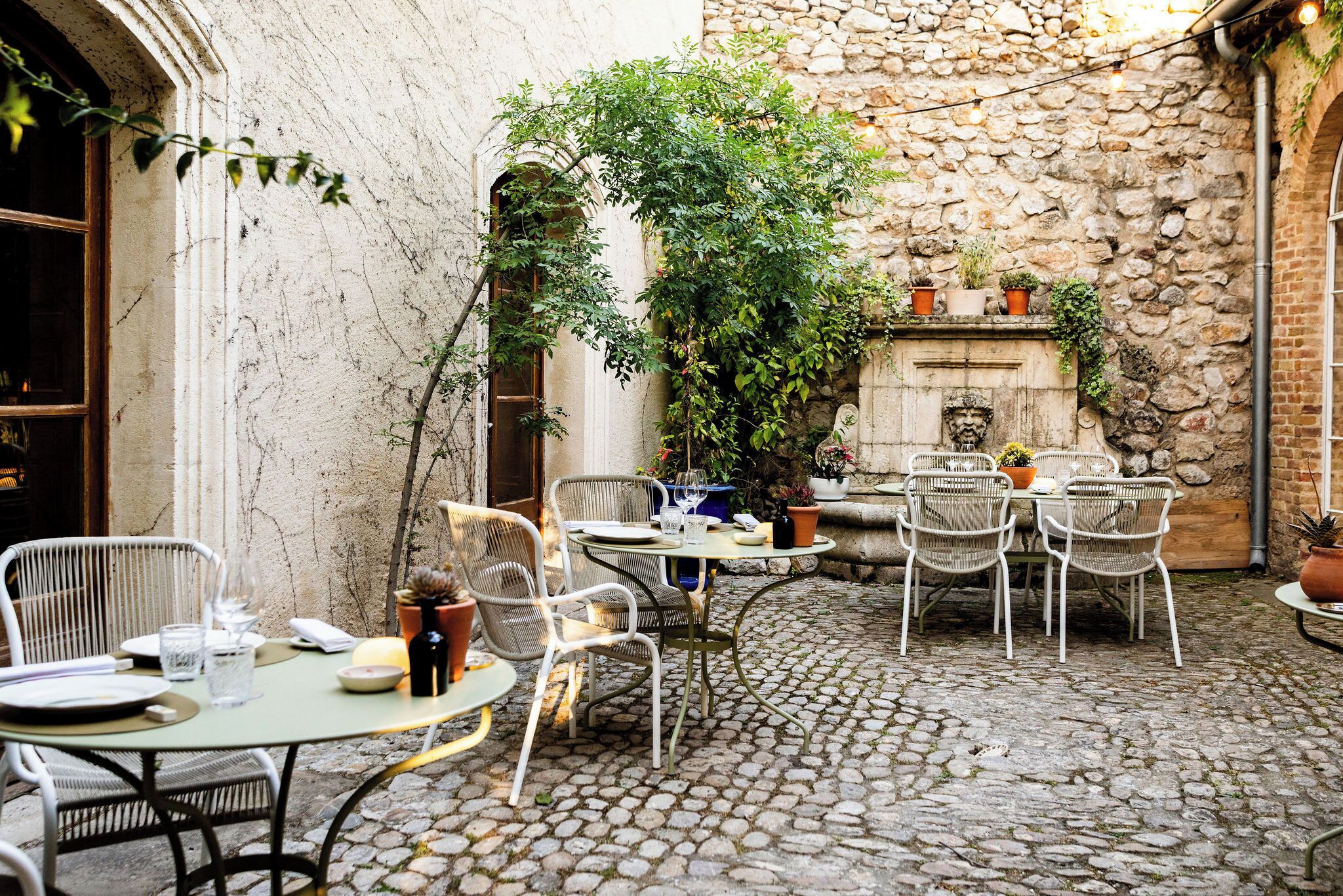 An outdoor patio with stone walls, wicker furniture, and potted plants.