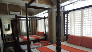 Ein Hotelzimmer mit vier Betten, die in einer U-Form angeordnet sind, jeweils mit einem hölzernen Gestell und orangener Bettwäsche.