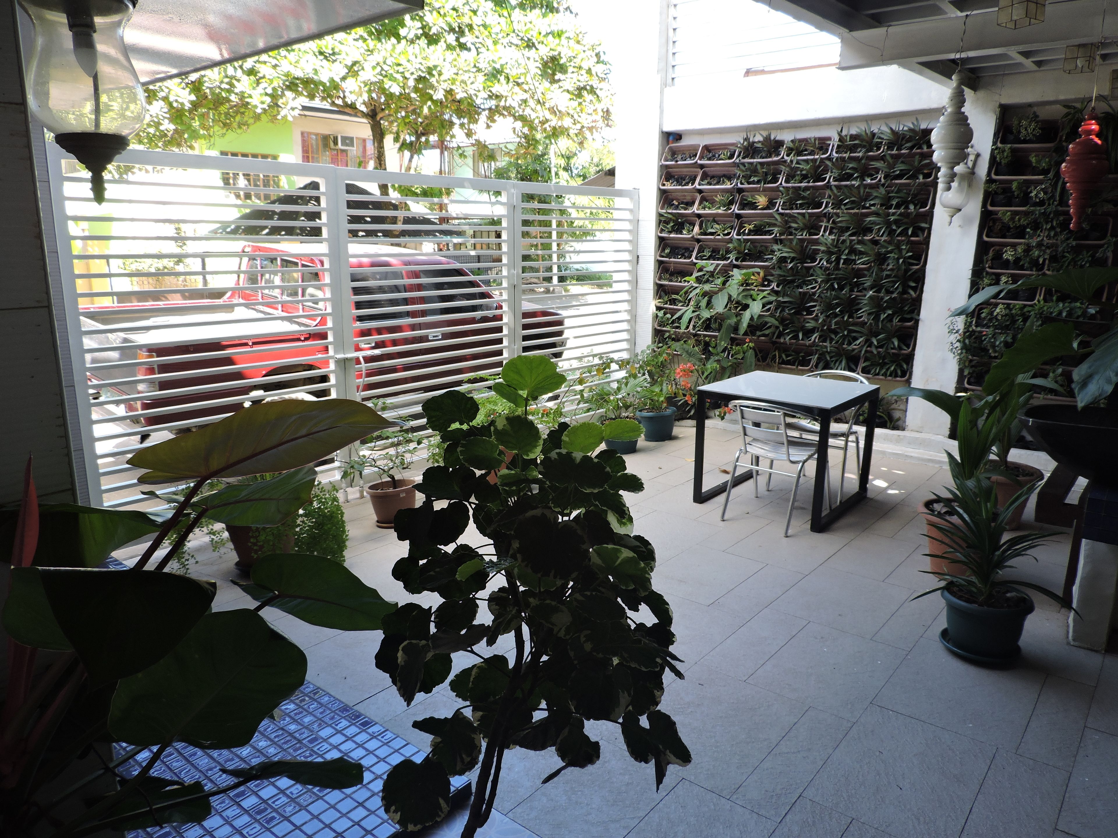 Un espace extérieur aménagé en patio, avec un sol carrelé, une table, des chaises et diverses plantes en pot.
