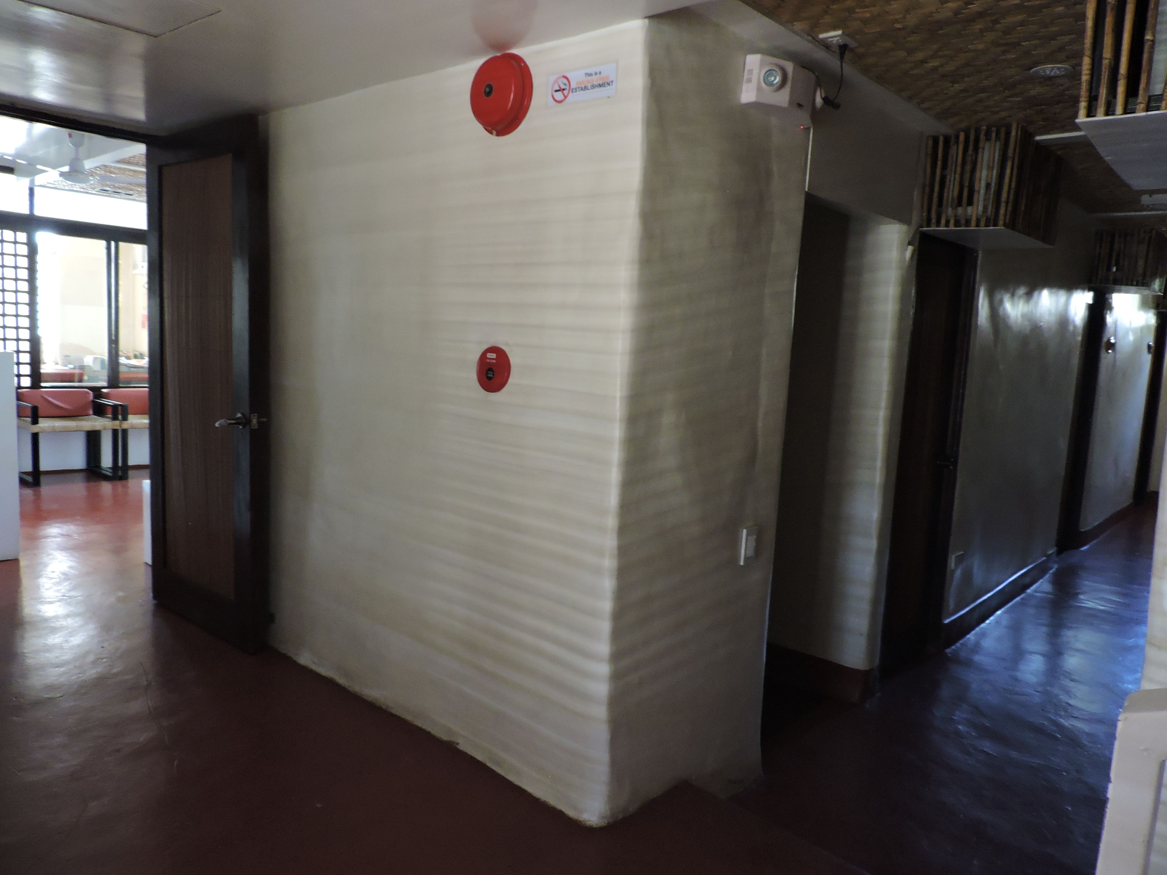 A hallway with a white textured wall, a red emergency pull station, and a stainless steel refrigerator.
