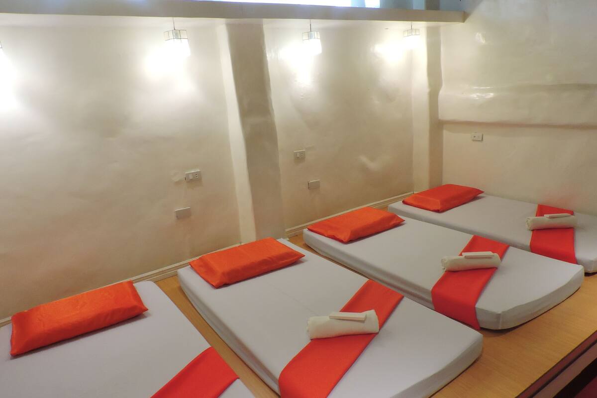 A row of massage therapy beds with orange headrests and white sheets, arranged in a treatment room with a plain wall and ceiling.