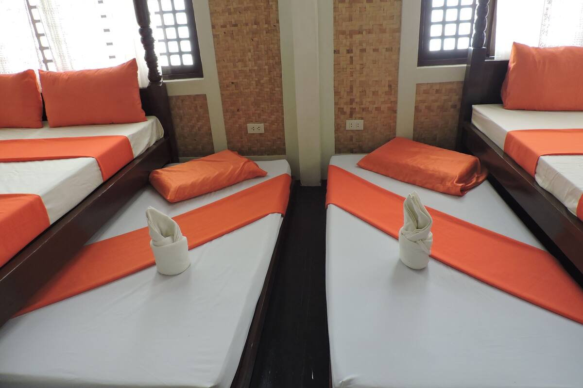 A hotel room with four single beds, each with an orange bedspread and matching pillows.