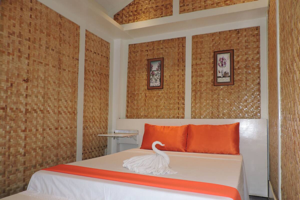 A hotel room with a bed, a small table, and two framed pictures on the wall.
