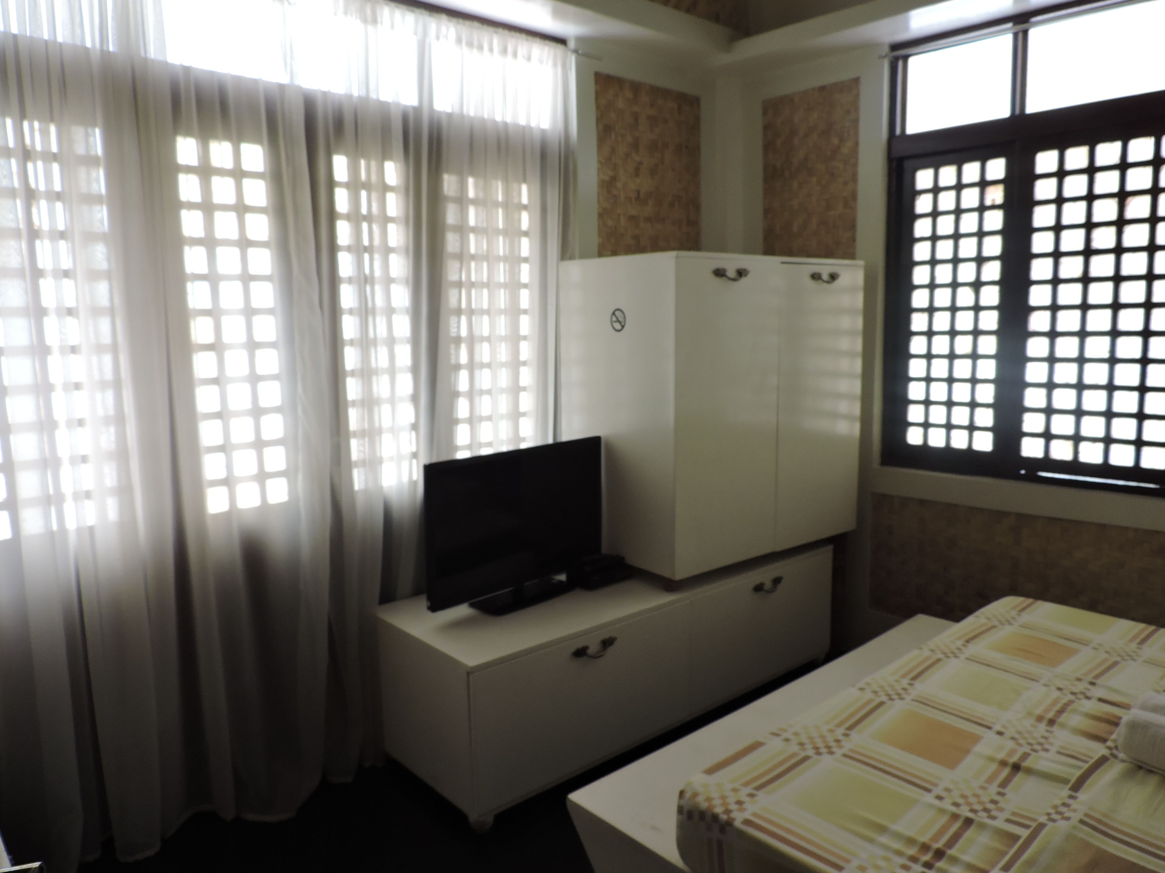 Una habitación con una cama, un televisor sobre un mueble y una ventana con diseño de cuadrícula.