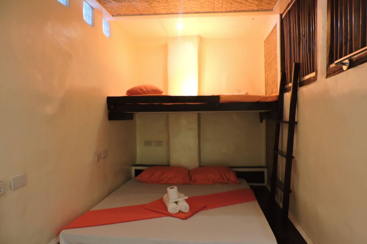 A bunk bed with a red blanket and pillows, a white mattress, and a teddy bear on the lower bed.