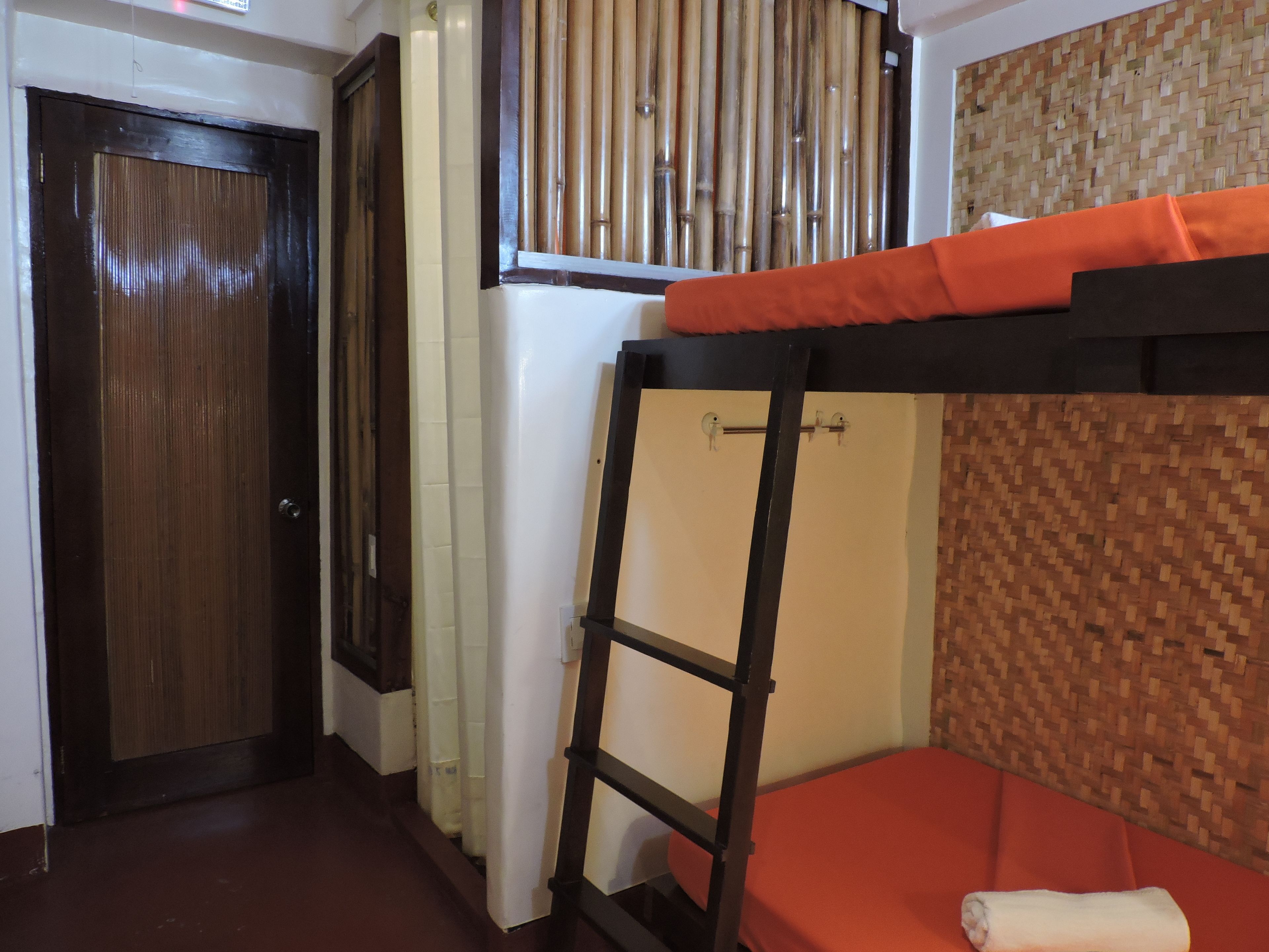 A room with a bunk bed, a wooden door, a bamboo wall, and a woven wall panel.