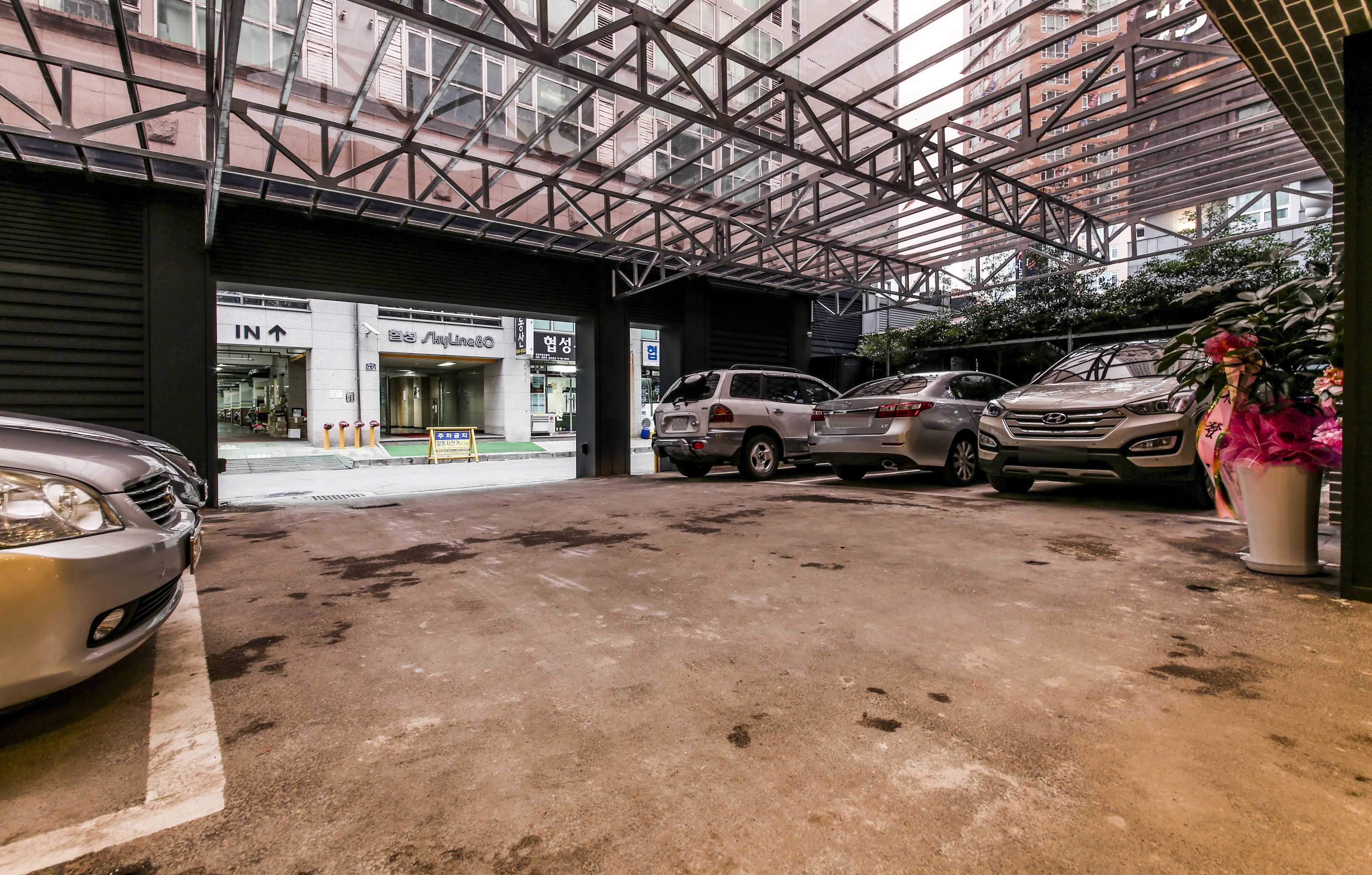 A parking area with a covered structure, a building entrance, and a car parked to the left.