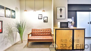 A reception area with a brown leather sofa, pendant lights, framed artwork, and a wooden counter with a microwave. - Ignis Hotel Busan Sports Complex Branch (Busan)