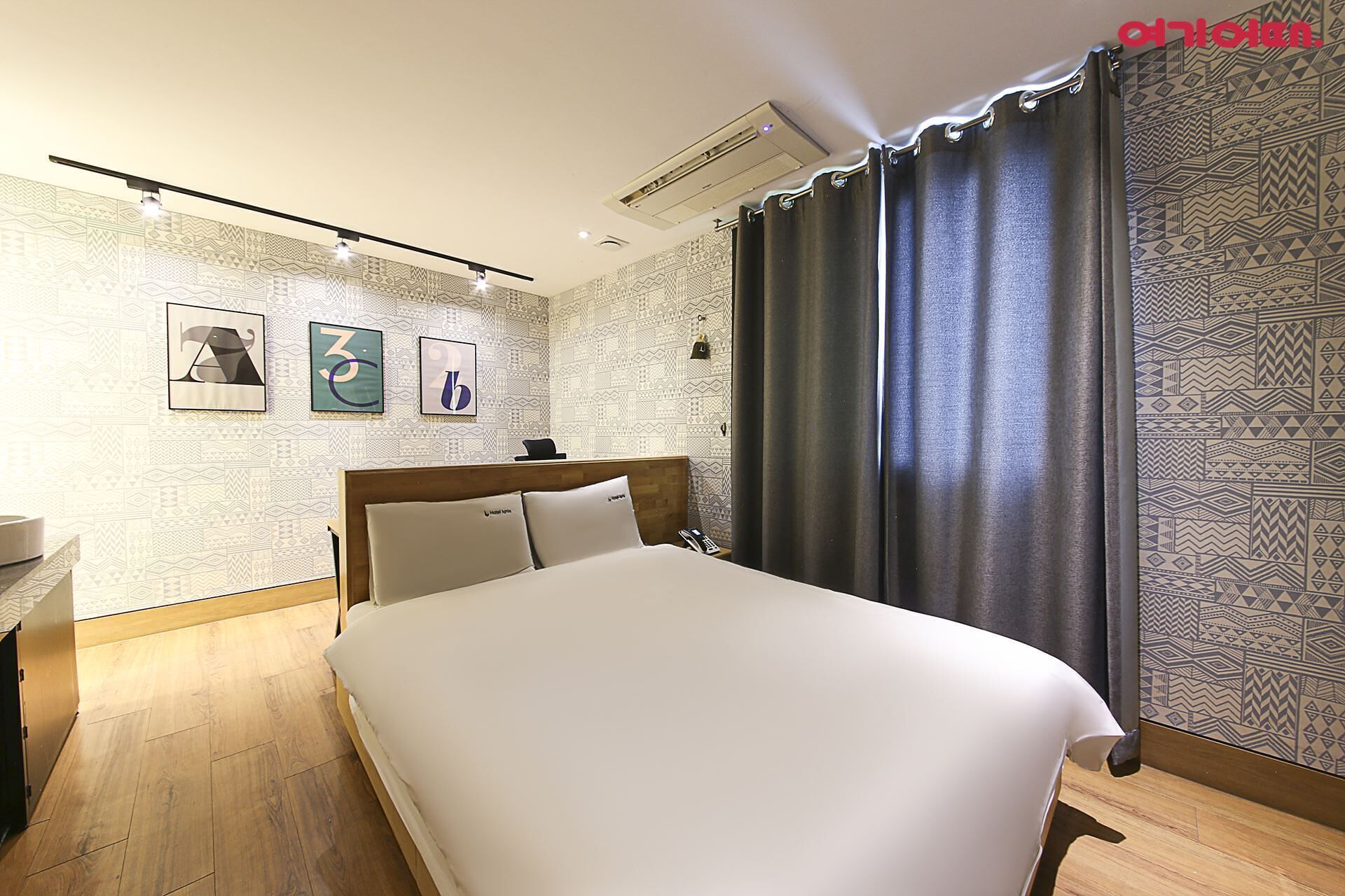 Una habitación de hotel con cama, mesita de noche, aire acondicionado de pared y cortinas estampadas.