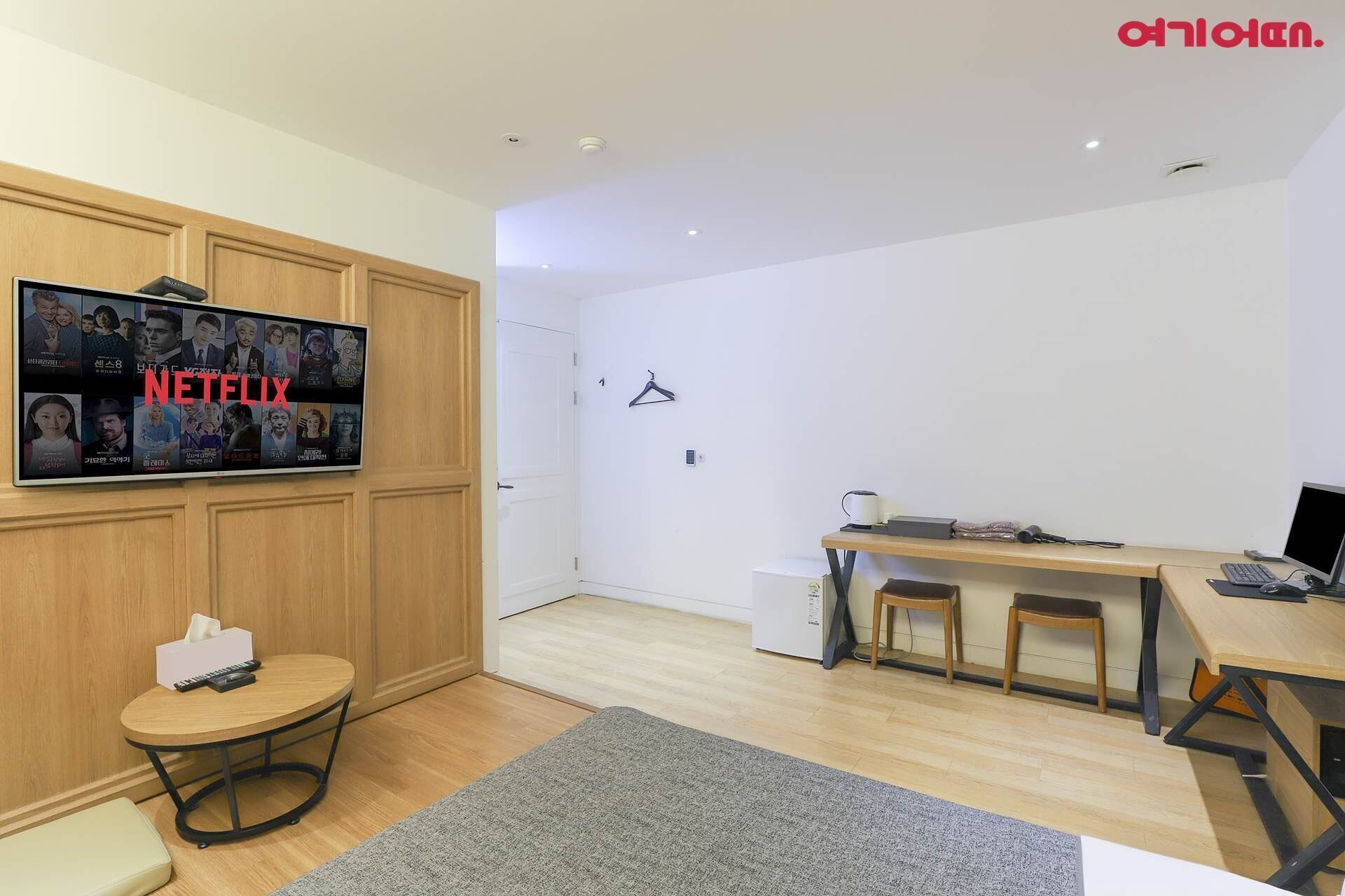 Une pièce moderne avec un meuble en bois, une table ronde sur laquelle se trouve un ordinateur portable, un petit tabouret et un tapis gris.