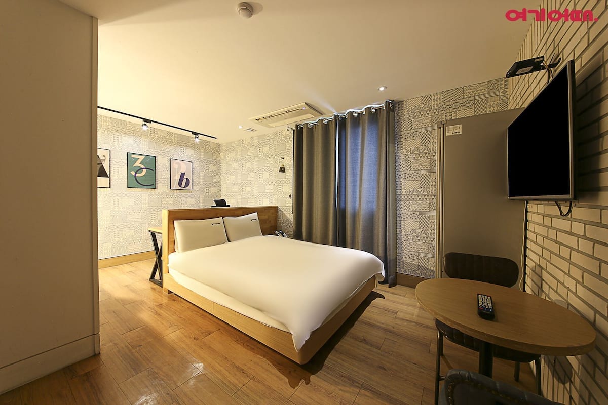 Une chambre d’hôtel avec un lit, un téléviseur fixé au mur, une petite table et une chaise.