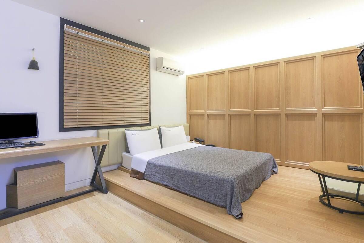 Une chambre à coucher avec un lit, un bureau avec un ordinateur, une armoire et une petite table.
