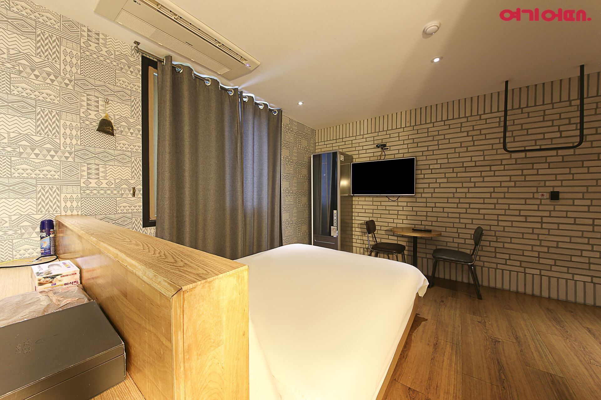 A hotel room with a bed, a desk, a chair, a TV, and a brick-patterned wall.