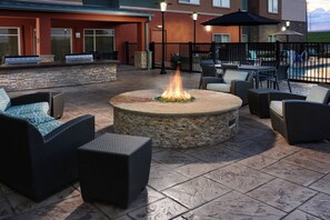 An outdoor patio area with a stone fire pit surrounded by wicker furniture and a pool in the background. - Residence Inn by Marriott Houston Pasadena (Pasadena)
