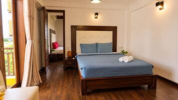 Habitación de hotel con cama de madera, mesita de noche, lámpara de noche y vistas al exterior.