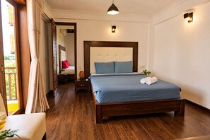A hotel room with a wooden bed, a nightstand, a bedside lamp, and a view of the outdoors. - Flower’s House Hoi An (Da Nang)