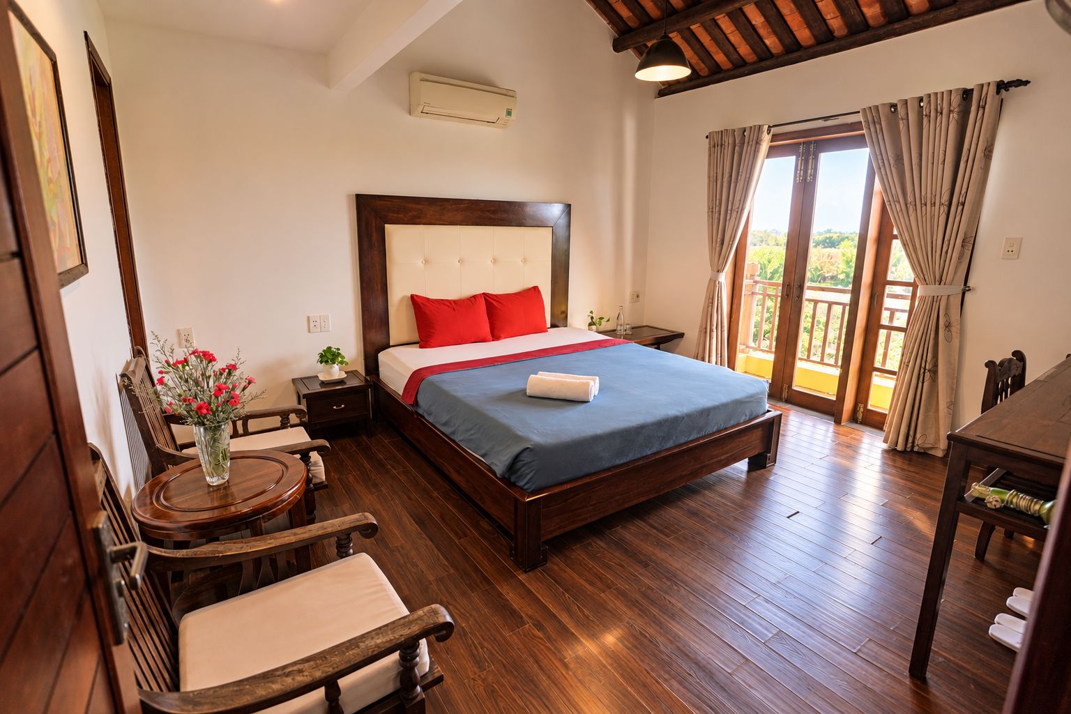 Habitación de hotel con cama de madera, mesita de noche, una silla, una pequeña mesa y vistas al exterior a través de una puerta corrediza.