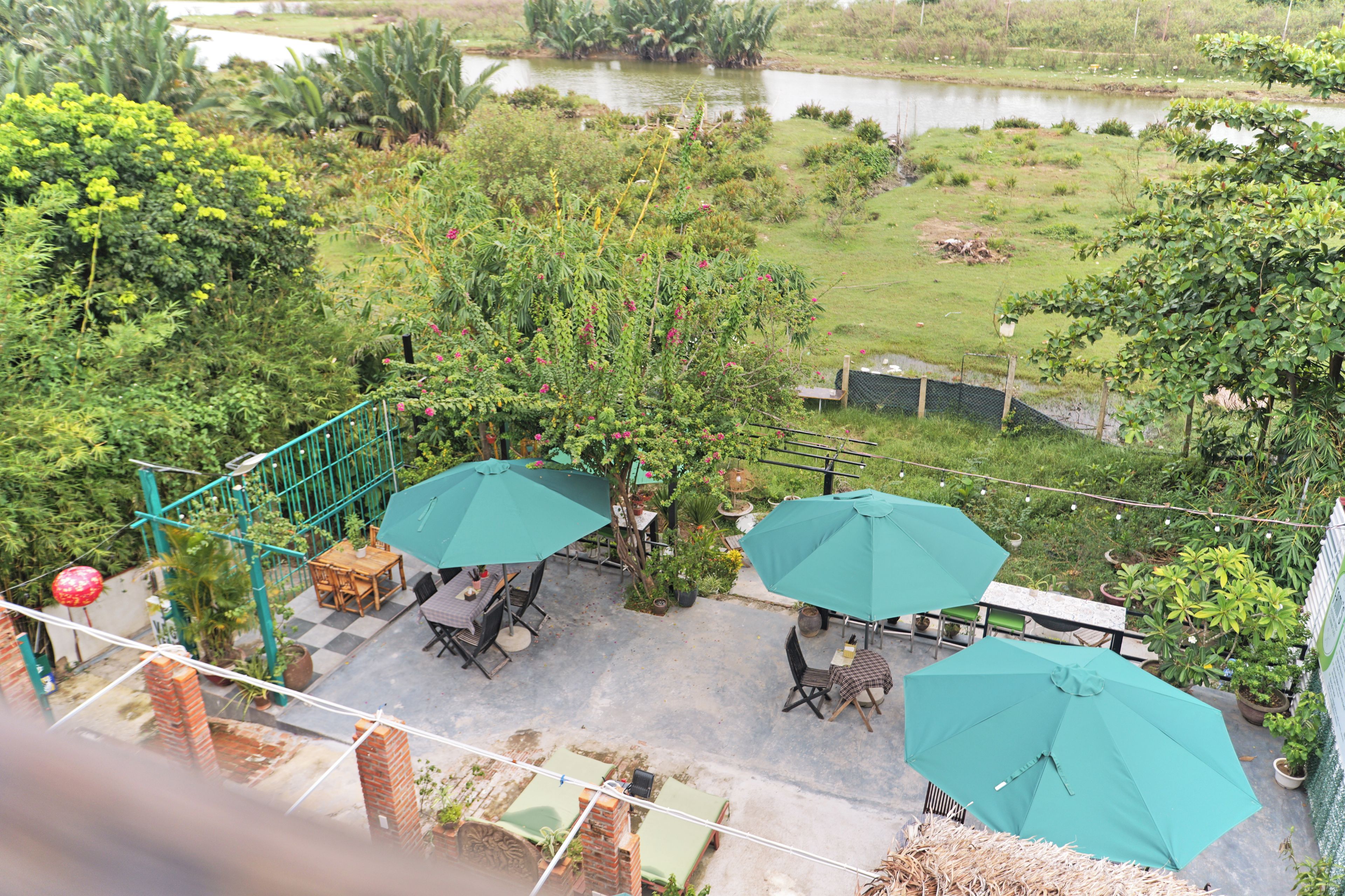 Área de pátio com mobiliário externo e guarda-sóis, com vista para um jardim com lago.