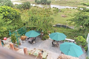 A patio area with outdoor seating and umbrellas, overlooking a garden with a pond. - Flower’s House Hoi An (Da Nang)