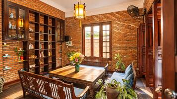 A room with a brick wall, wooden furniture, a table with chairs, a bookshelf, and a hanging fan.